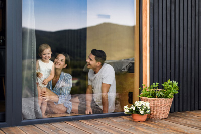 A happy family, husband, wife, and child, standing in front of their home window, showcasing the benefits of a Home Equity Line of Credit (HELOC).