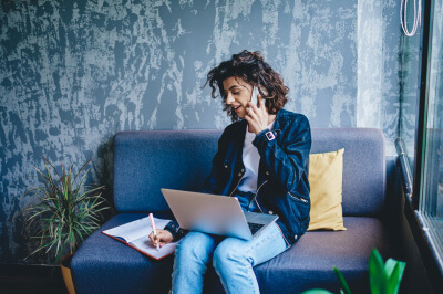 Woman with laptop on her cell phone prepares for mortgage rates to drop.