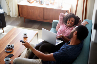 Couple relaxing on couch with laptop researches down payment assistance.